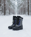 Pair of gray winter boots with blue accents on a snowy forest floor.
